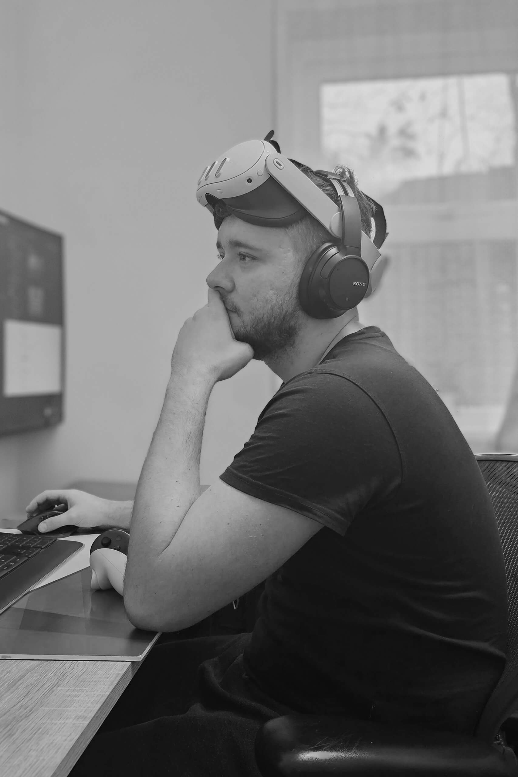 Krystian wearing a VR headset and headphones, sitting at a desk and working on 3D Visualization